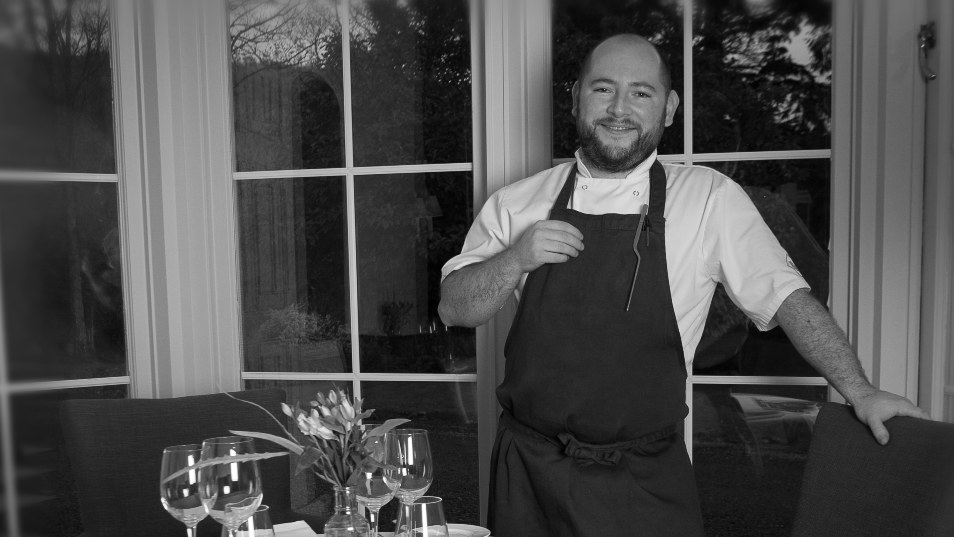 Black and white photo of a man in chef whites by a set table