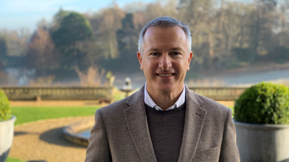 Image of an older man in a tweed suit standing outside of a hotel