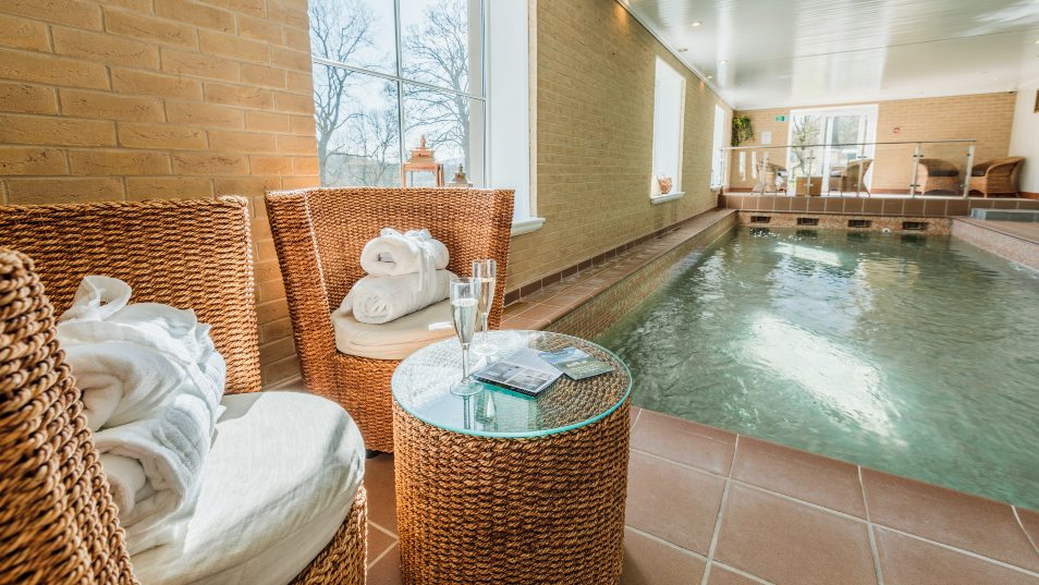 Image of 2 wicker chairs with towels on by an indoor pool